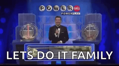A Man In A Tuxedo Is Holding A Microphone In Front Of A Powerball Lottery Machine . GIF