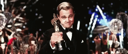 A Man In A Tuxedo Is Holding An Oscar In His Hand . GIF