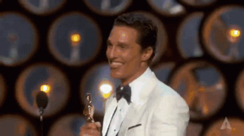 a man in a tuxedo is holding an oscar trophy on a stage and smiling .