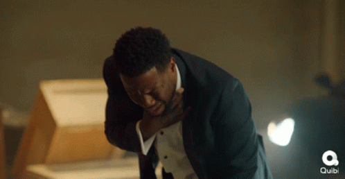 A Man In A Tuxedo Is Holding His Chest In Pain And The Word Quibi Is Visible In The Background GIF