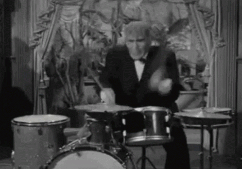 A Man In A Tuxedo Is Playing The Drums In A Black And White Photo . GIF