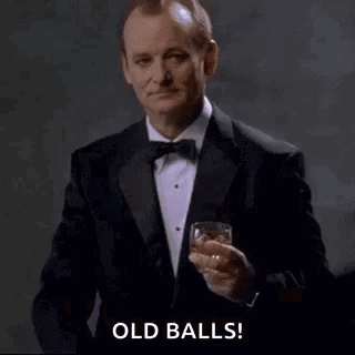 A Man In A Tuxedo Is Pointing At The Camera While Holding A Glass Of Whiskey . GIF