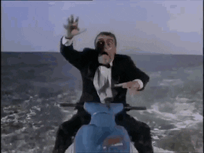 A Man In A Tuxedo Is Riding A Blue Scooter On Top Of A Mountain . GIF