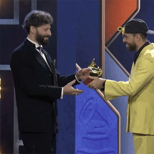 A Man In A Tuxedo Is Shaking Hands With Another Man In A Yellow Suit GIF