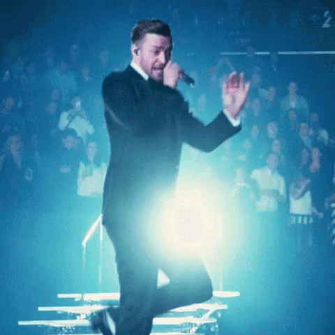 A Man In A Tuxedo Is Singing Into A Microphone In Front Of A Crowd GIF