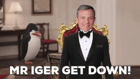 A Man In A Tuxedo Is Sitting In A Chair With The Words Mr Iger Get Down Behind Him GIF
