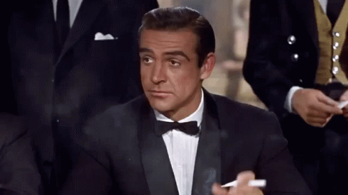 A Man In A Tuxedo Is Smoking A Cigarette And Looking At Something GIF