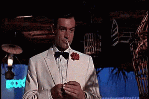 A Man In A Tuxedo Is Smoking A Cigarette In A Dark Room . GIF