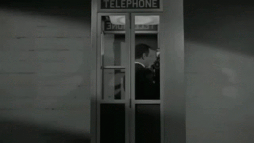 A Man In A Tuxedo Is Standing In A Telephone Booth In A Black And White Photo . GIF