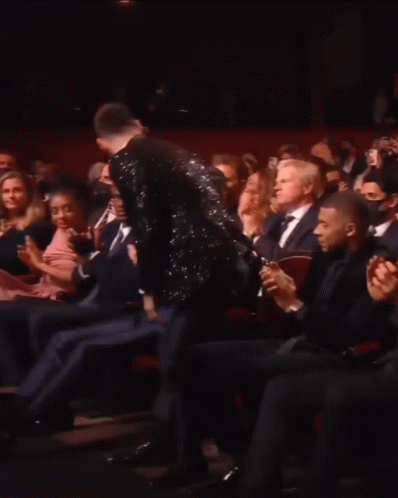 A Man In A Tuxedo Is Standing In Front Of A Crowd Applauding GIF