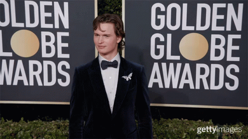 a man in a tuxedo is standing in front of a sign that says golden globe awards