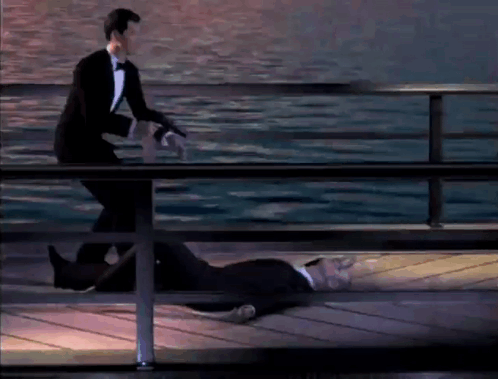 A Man In A Tuxedo Is Standing Next To A Dead Man On A Pier GIF