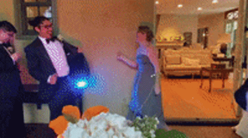 A Man In A Tuxedo Is Standing Next To A Woman In A Blue Dress In A Living Room GIF
