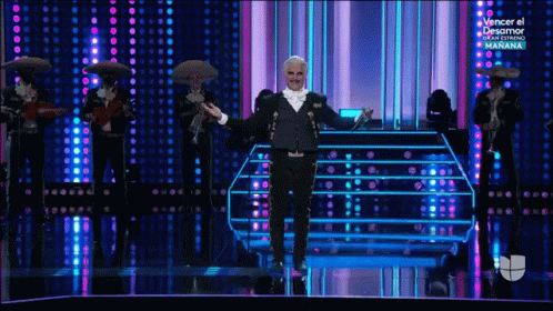 a man in a tuxedo is standing on a stage with mariachi players behind him
