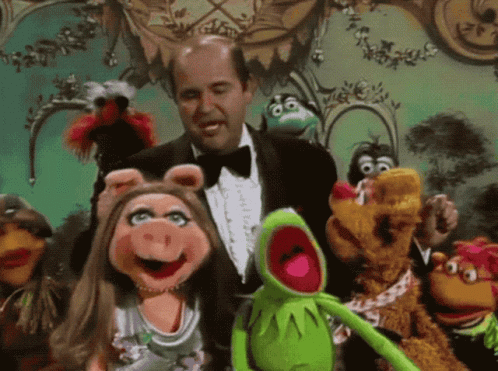 A Man In A Tuxedo Is Surrounded By Muppets Including Kermit GIF