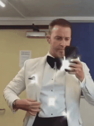 A Man In A Tuxedo Is Taking A Picture Of Himself In A Mirror GIF