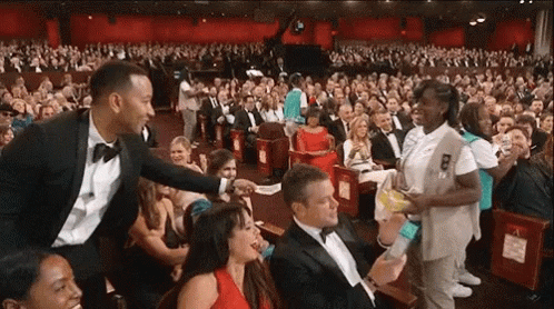 A Man In A Tuxedo Is Talking To A Girl Scout In A Crowd GIF