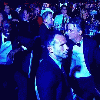 A Man In A Tuxedo Is Talking To Another Man In A Crowd Of People GIF