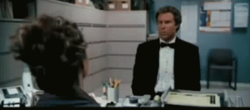 A Man In A Tuxedo Is Talking To Another Man In A Cubicle GIF