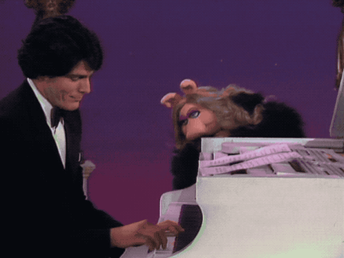 A Man In A Tuxedo Plays A Piano Next To A Stuffed Pig GIF