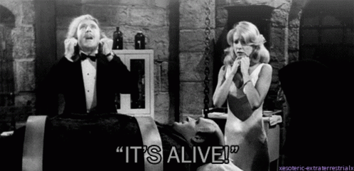 A Man In A Tuxedo Says " It 'S Alive " In Front Of A Woman In A White Dress GIF