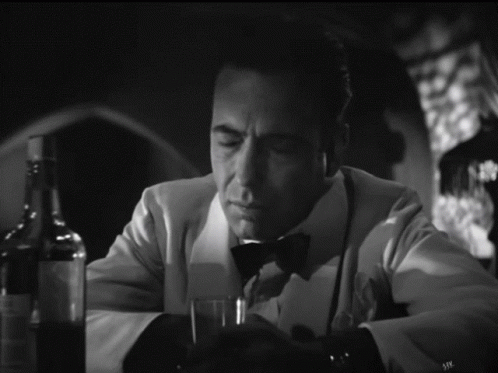 a man in a tuxedo sits at a table with a glass of wine