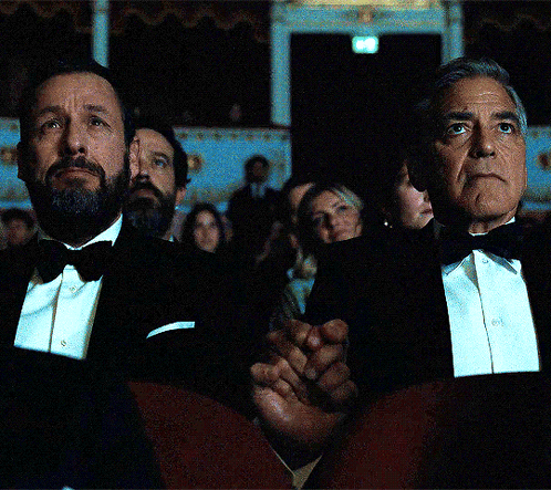 a man in a tuxedo sits next to another man in a tuxedo