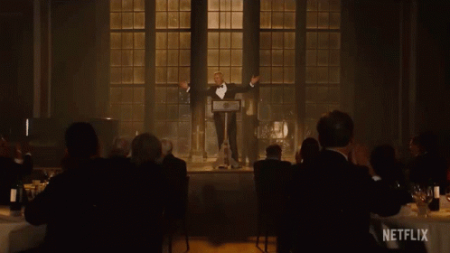 A Man In A Tuxedo Stands At A Podium In Front Of A Crowd With A Netflix Logo In The Corner GIF