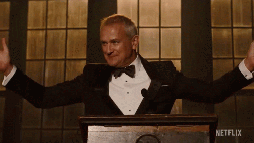 A Man In A Tuxedo Stands Behind A Podium With Netflix Written On The Bottom GIF