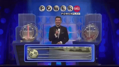 A Man In A Tuxedo Stands In Front Of A Powerball Lottery Machine GIF