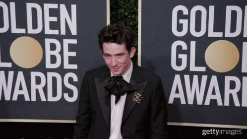 A Man In A Tuxedo Stands In Front Of A Sign That Says Golden Globes GIF