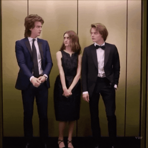 A Man In A Tuxedo Stands Next To A Woman In A Black Dress And A Man In A Bow Tie GIF