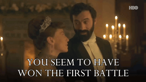 A Man In A Tuxedo Stands Next To A Woman In A Tiara With The Words You Seem To Have Won The First Battle GIF