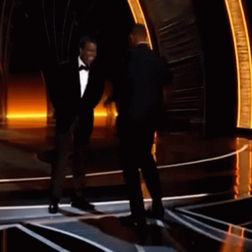 A Man In A Tuxedo Stands Next To Another Man In A Tuxedo On A Stage GIF