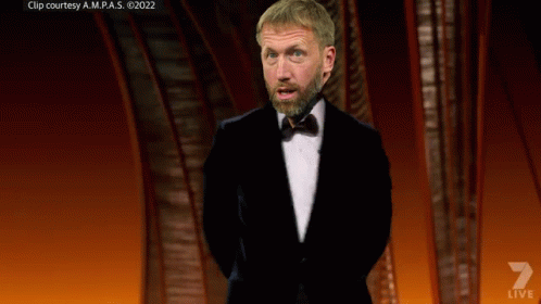 A Man In A Tuxedo Stands On A Stage With A Shield That Says Arsenal GIF