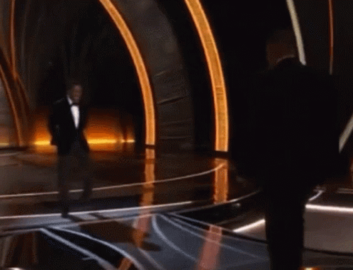 A Man In A Tuxedo Stands On A Stage With Another Man GIF