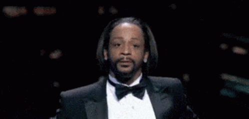 A Man In A Tuxedo With A Beard Is Making A Funny Face . GIF