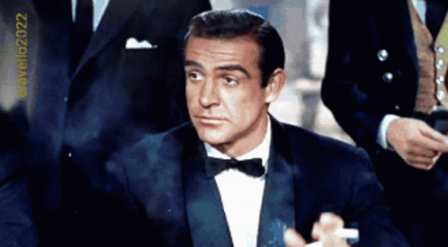 A Man In A Tuxedo With A Bow Tie Is Standing In Front Of A Sign That Says Cravello2022 GIF