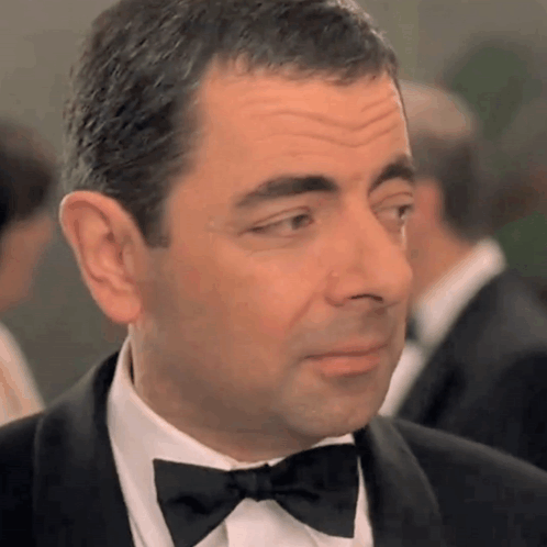 A Man In A Tuxedo With A Bow Tie Looks At The Camera GIF