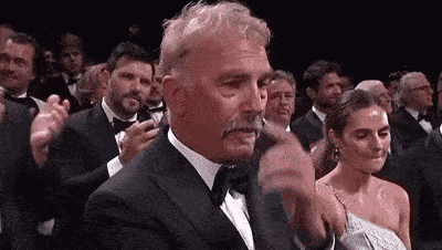 A Man In A Tuxedo With A Mustache Is Applauding In A Crowd . GIF