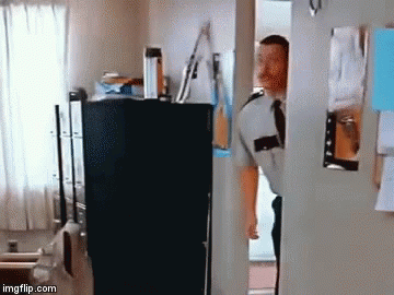A Man In A Uniform And Tie Is Standing In A Doorway Looking Into A Room . GIF