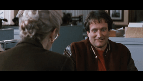 A Man In A Varsity Jacket Is Smiling While Talking To A Woman GIF