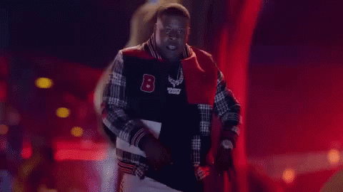 a man in a varsity jacket is standing in front of the word pop it