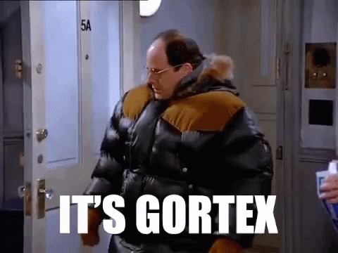 A Man In A Very Large Jacket Is Standing In Front Of A Door . GIF