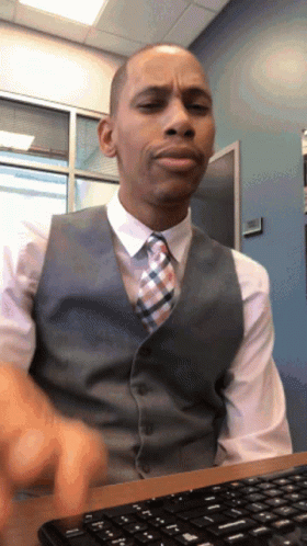 A Man In A Vest And Tie Sits At A Desk With A Keyboard GIF