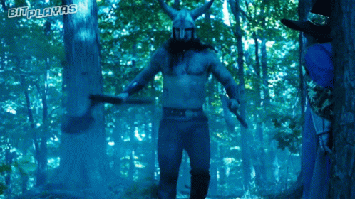 A Man In A Viking Costume Is Holding A Axe In A Forest With The Words Bi-Playas Written Above Him GIF