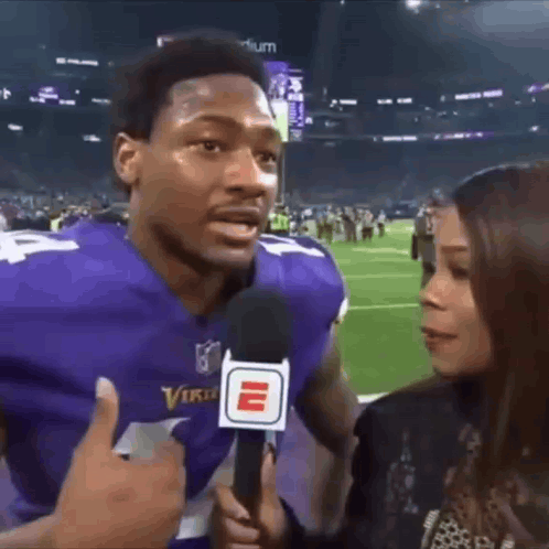 A Man In A Vikings Jersey Is Being Interviewed By A Woman . GIF