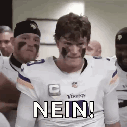 A Man In A Vikings Jersey Is Standing In Front Of A Group Of Men With Face Paint On Their Faces . GIF