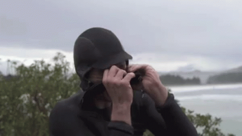 A Man In A Wetsuit Is Taking A Picture Of A Body Of Water . GIF