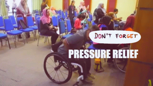 A Man In A Wheelchair Is Sitting In A Room With People Sitting In Chairs And A Sign That Says Pressure Relief GIF